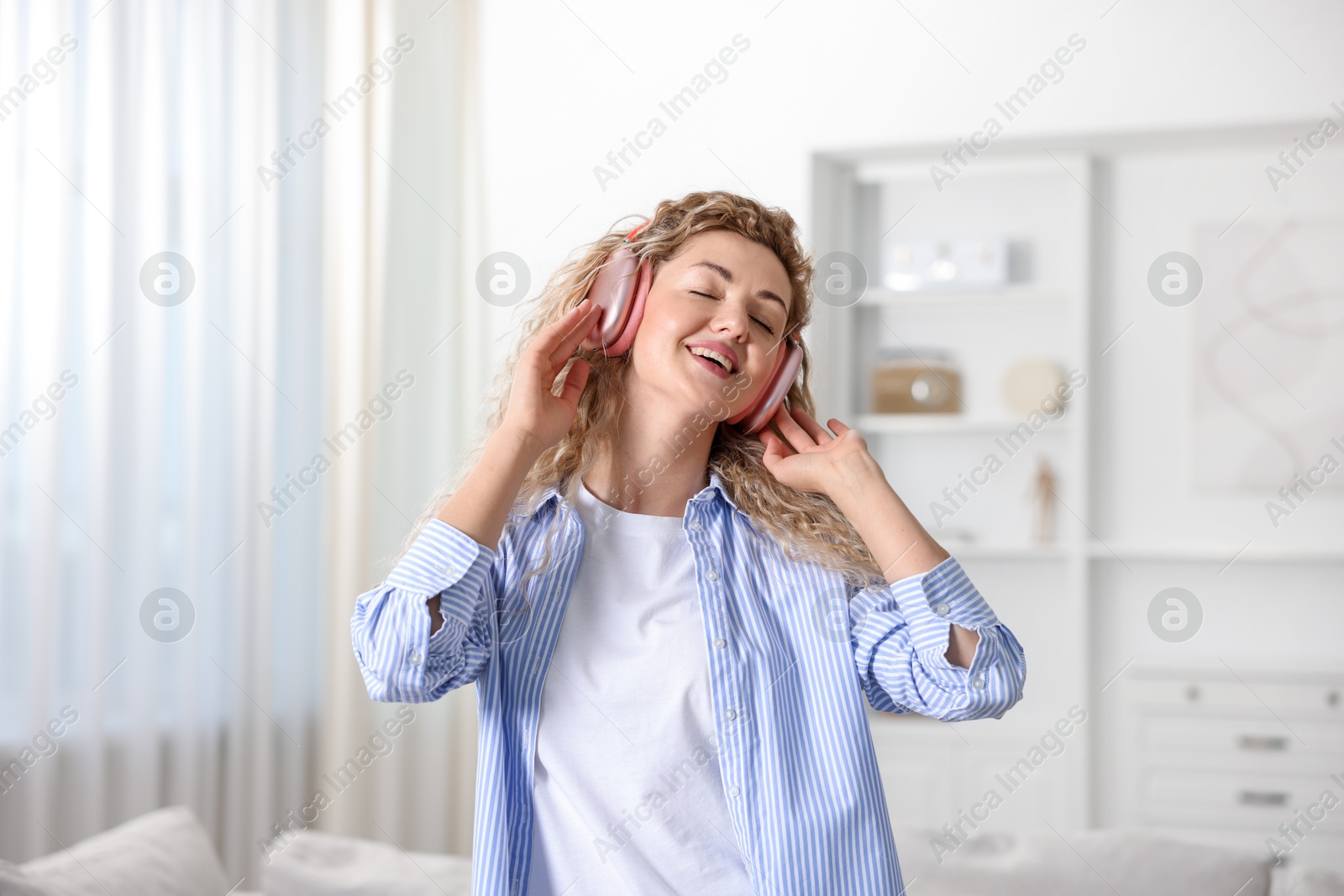Photo of Happy woman in headphones listening to music and dancing at home