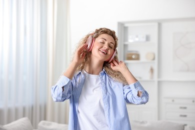 Photo of Happy woman in headphones listening to music and dancing at home