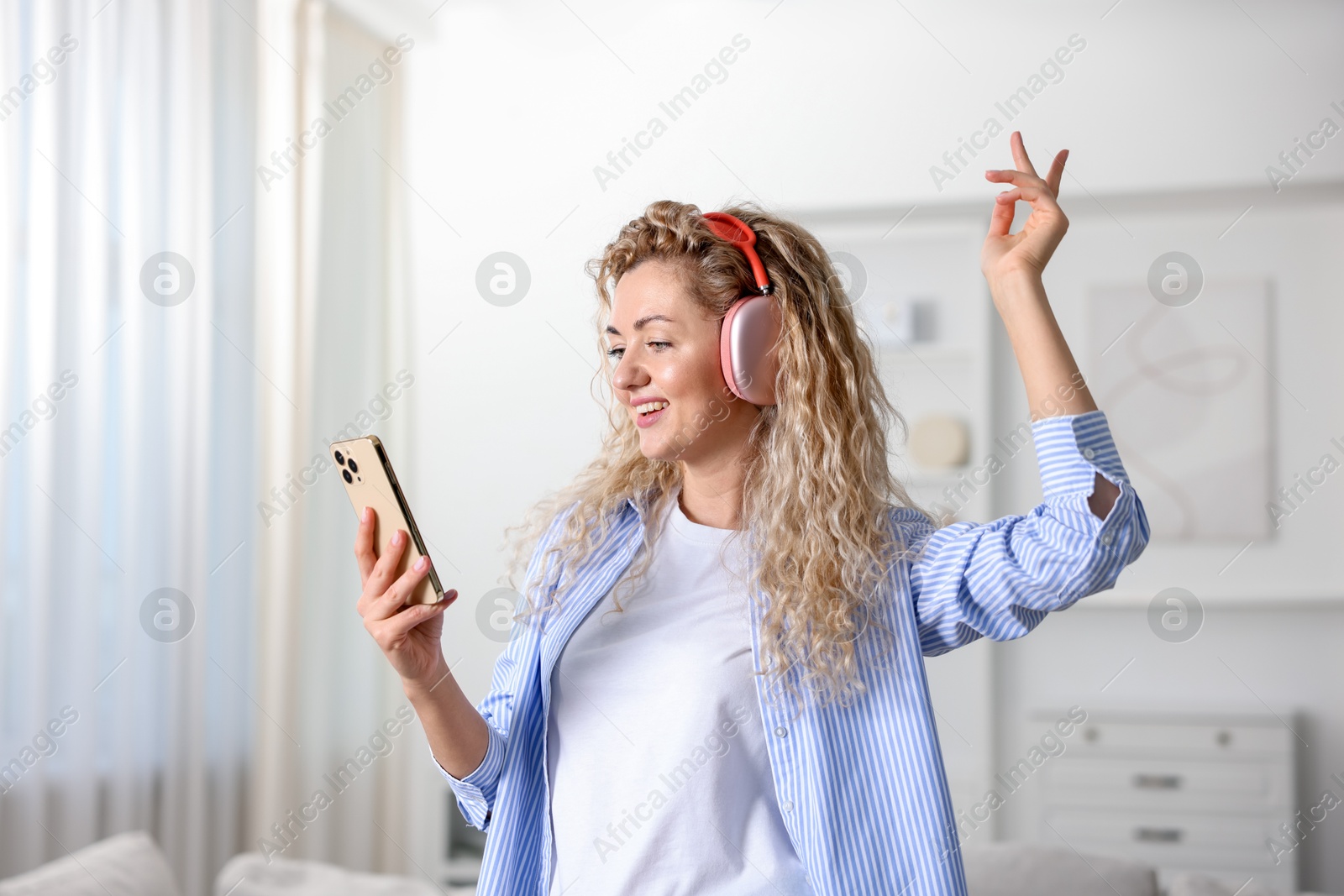Happy woman with smartphone listening to music in headphones at home Photo of Happy woman with smartphone listening to music in headphones at home