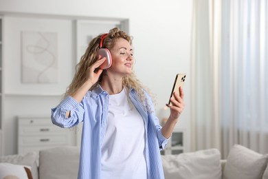 Photo of Happy woman with smartphone listening to music in headphones at home