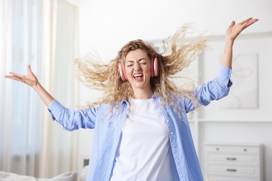 Photo of Happy woman in headphones listening to music and dancing at home