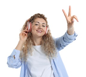 Photo of Happy woman listening to music in headphones and showing peace sign on white background