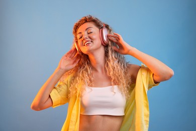 Photo of Happy woman listening to music in headphones and dancing on light blue background