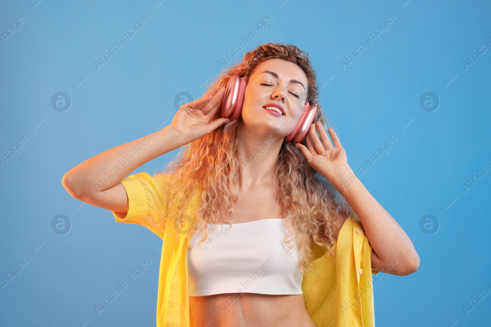 Happy woman listening to music in headphones and dancing on light blue background Photo of Happy woman listening to music in headphones and dancing on light blue background