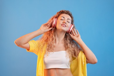 Photo of Happy woman listening to music in headphones and dancing on light blue background