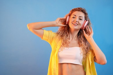 Photo of Happy woman listening to music in headphones and dancing on light blue background. Space for text
