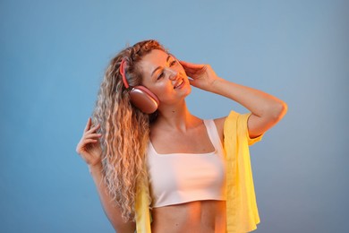 Photo of Happy woman listening to music in headphones and dancing on light blue background