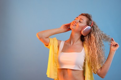 Photo of Happy woman listening to music in headphones and dancing on light blue background. Space for text