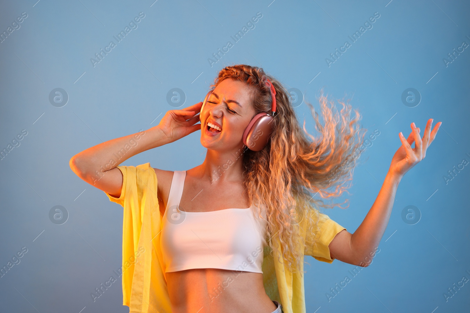 Happy woman listening to music in headphones and dancing on light blue background Photo of Happy woman listening to music in headphones and dancing on light blue background