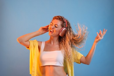 Photo of Happy woman listening to music in headphones and dancing on light blue background
