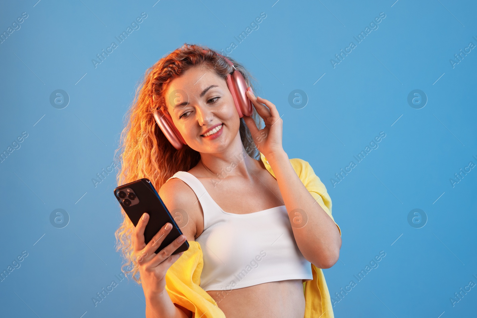 Photo of Happy woman with smartphone listening to music in headphones on light blue background
