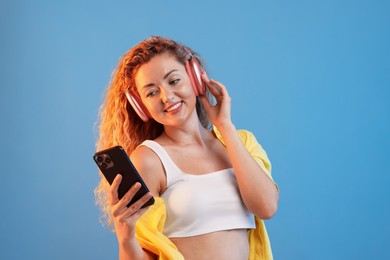 Photo of Happy woman with smartphone listening to music in headphones on light blue background