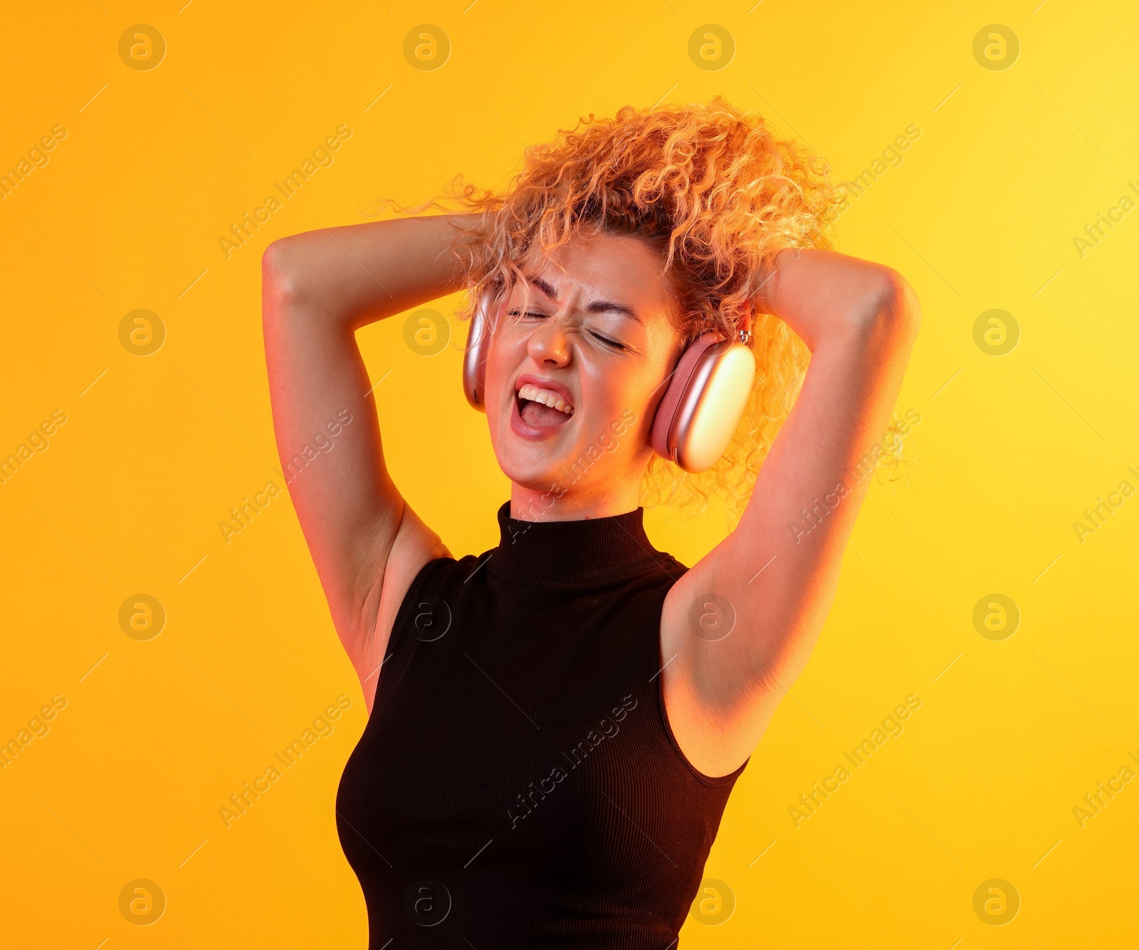 Happy woman listening to music in headphones and dancing on yellow background Photo of Happy woman listening to music in headphones and dancing on yellow background