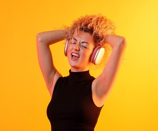 Photo of Happy woman listening to music in headphones and dancing on yellow background
