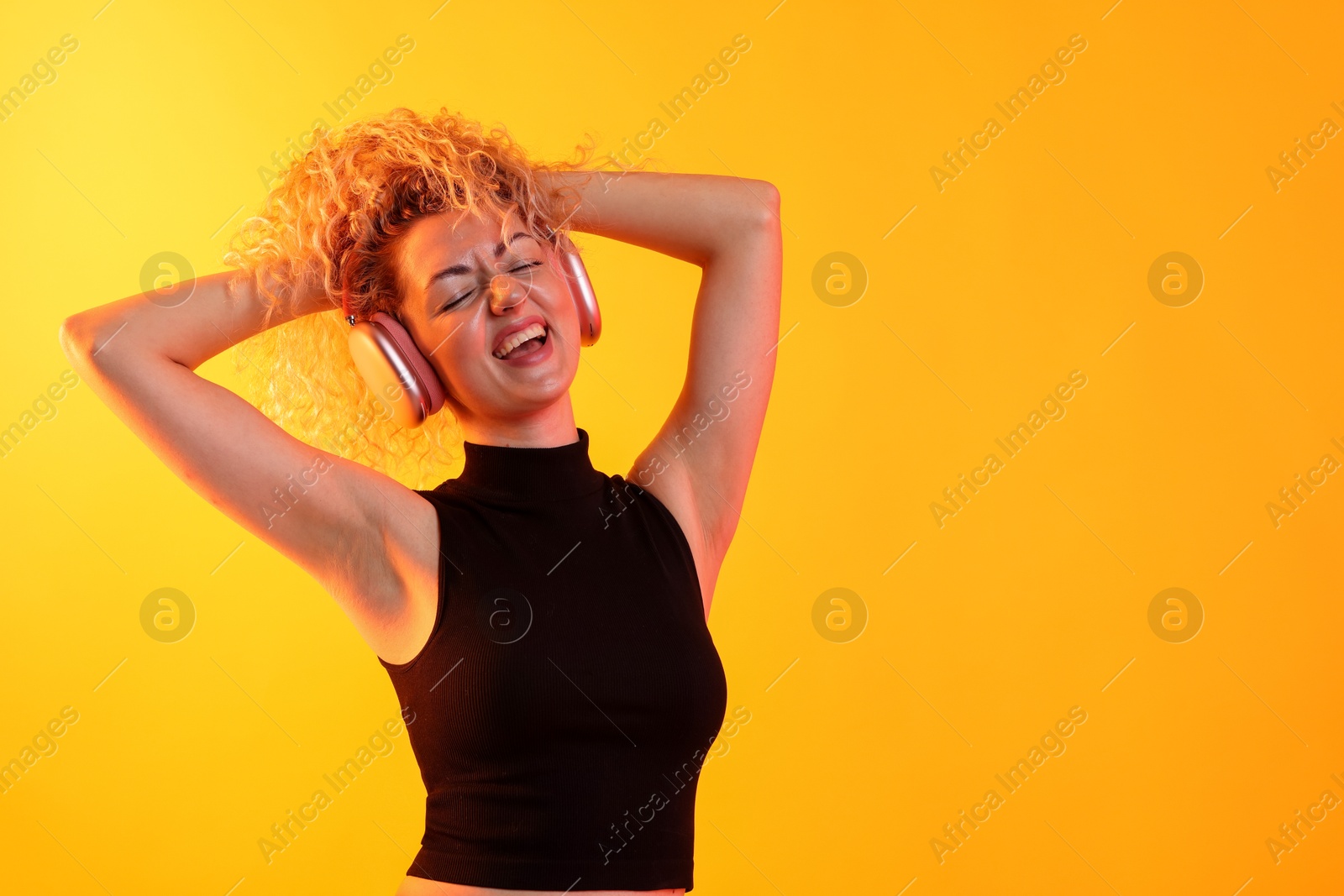 Happy woman listening to music in headphones and dancing on yellow background. Space for text Photo of Happy woman listening to music in headphones and dancing on yellow background. Space for text