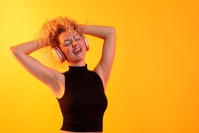 Photo of Happy woman listening to music in headphones and dancing on yellow background. Space for text