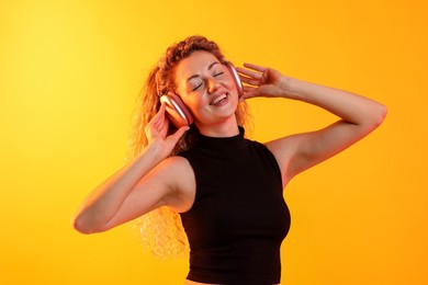 Photo of Happy woman listening to music in headphones and dancing on yellow background