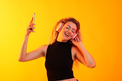Photo of Happy woman with smartphone listening to music in headphones on yellow background