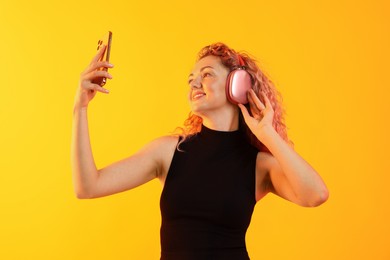 Photo of Happy woman with smartphone listening to music in headphones on yellow background