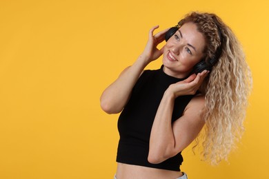 Photo of Happy woman listening to music in headphones and dancing on yellow background. Space for text