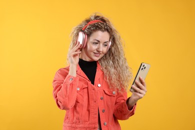 Photo of Happy woman with smartphone listening to music in headphones on yellow background