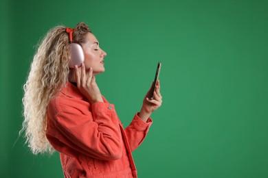 Photo of Happy woman with smartphone listening to music in headphones on green background. Space for text