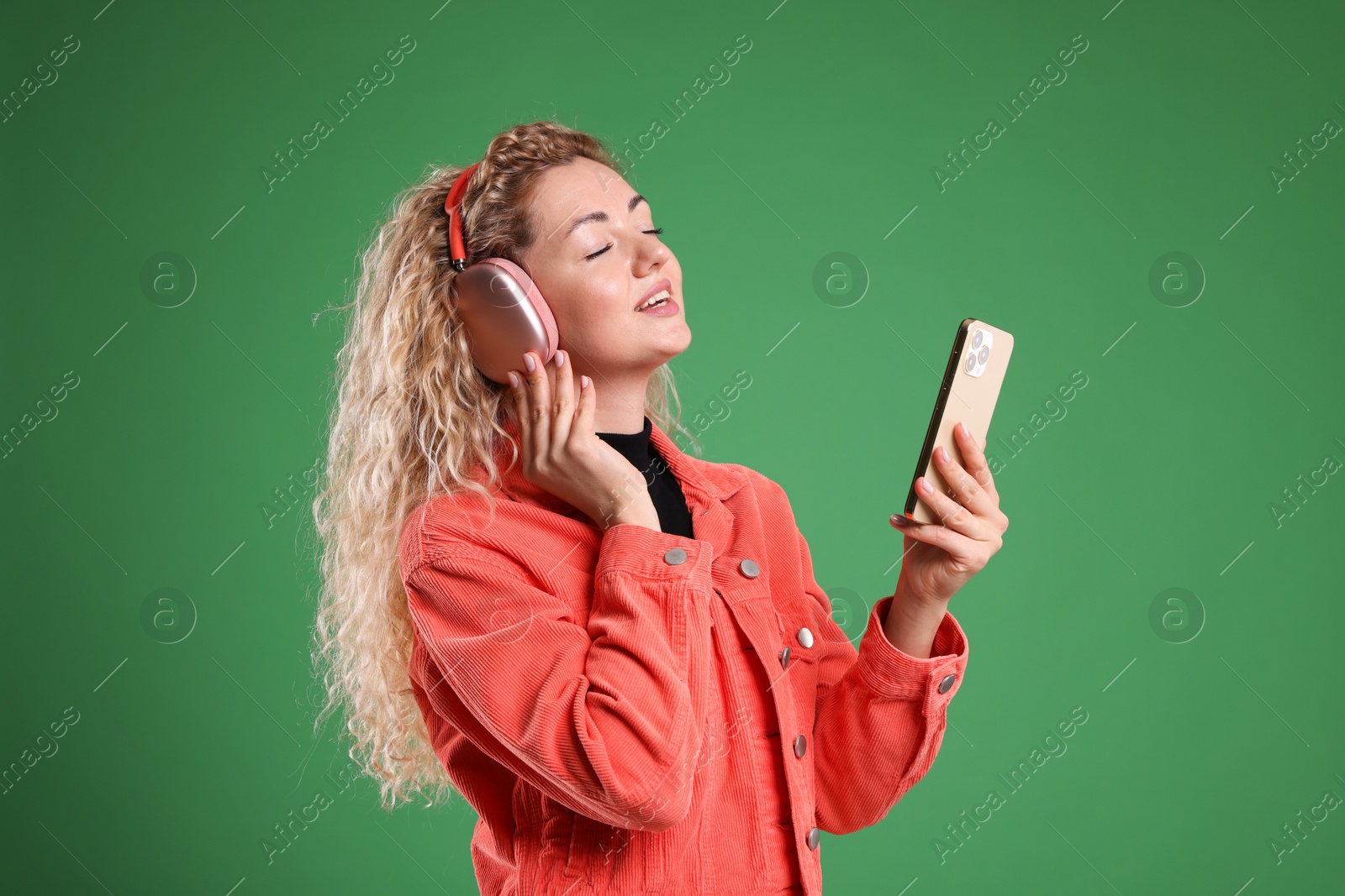 Happy woman with smartphone listening to music in headphones on green background Photo of Happy woman with smartphone listening to music in headphones on green background