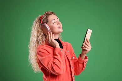 Photo of Happy woman with smartphone listening to music in headphones on green background