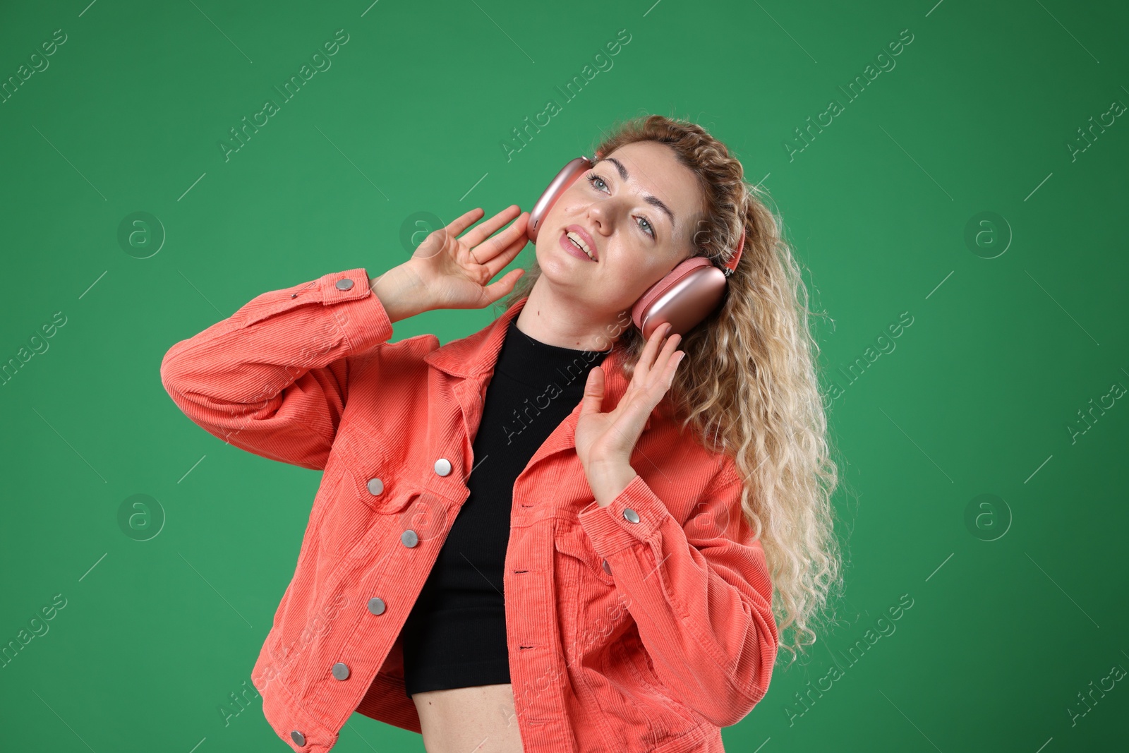 Happy woman listening to music in headphones and dancing on green background Photo of Happy woman listening to music in headphones and dancing on green background