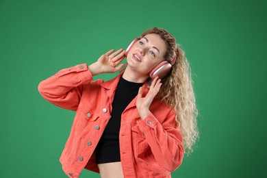 Photo of Happy woman listening to music in headphones and dancing on green background