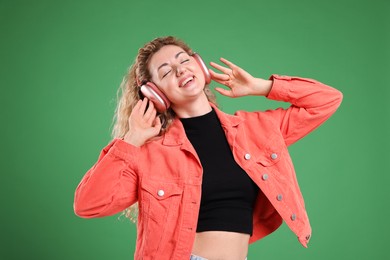 Photo of Happy woman listening to music in headphones and dancing on green background