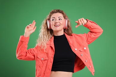 Photo of Happy woman listening to music in headphones and dancing on green background