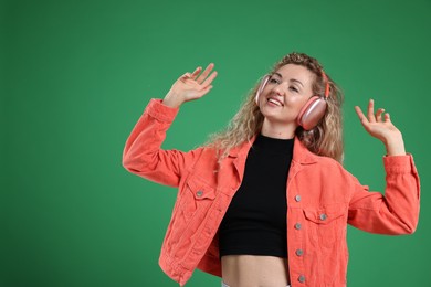 Photo of Happy woman listening to music in headphones and dancing on green background. Space for text