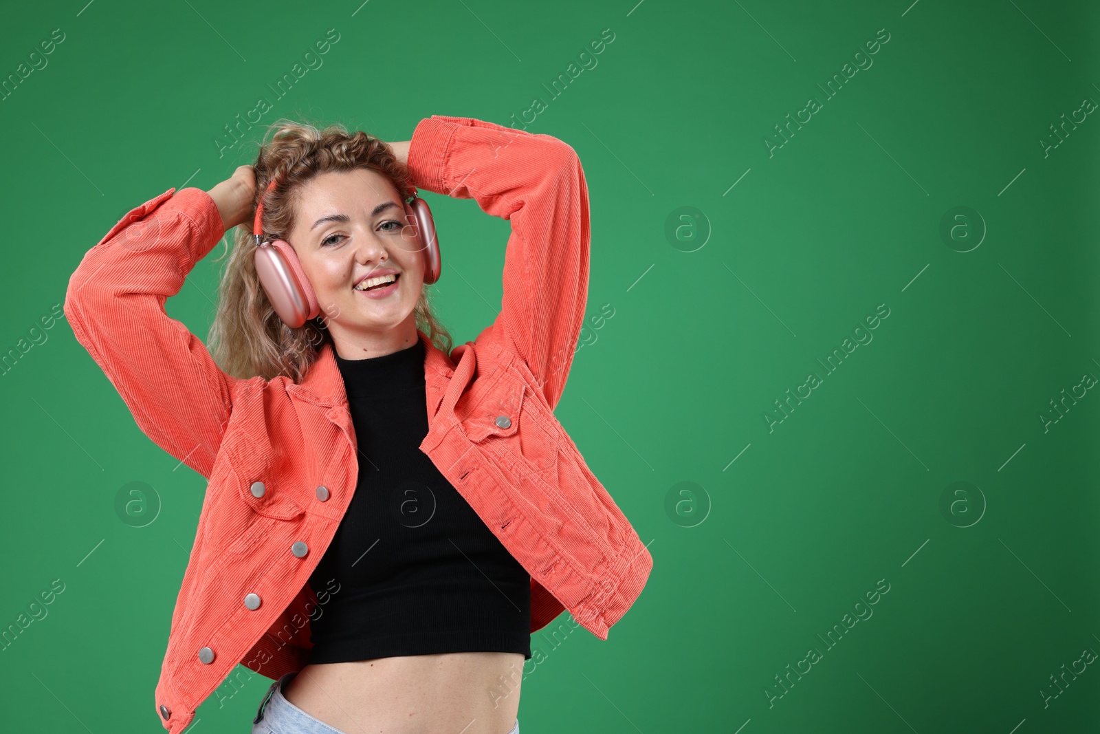 Happy woman listening to music in headphones and dancing on green background. Space for text Photo of Happy woman listening to music in headphones and dancing on green background. Space for text