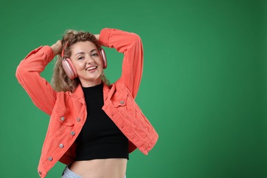 Photo of Happy woman listening to music in headphones and dancing on green background. Space for text
