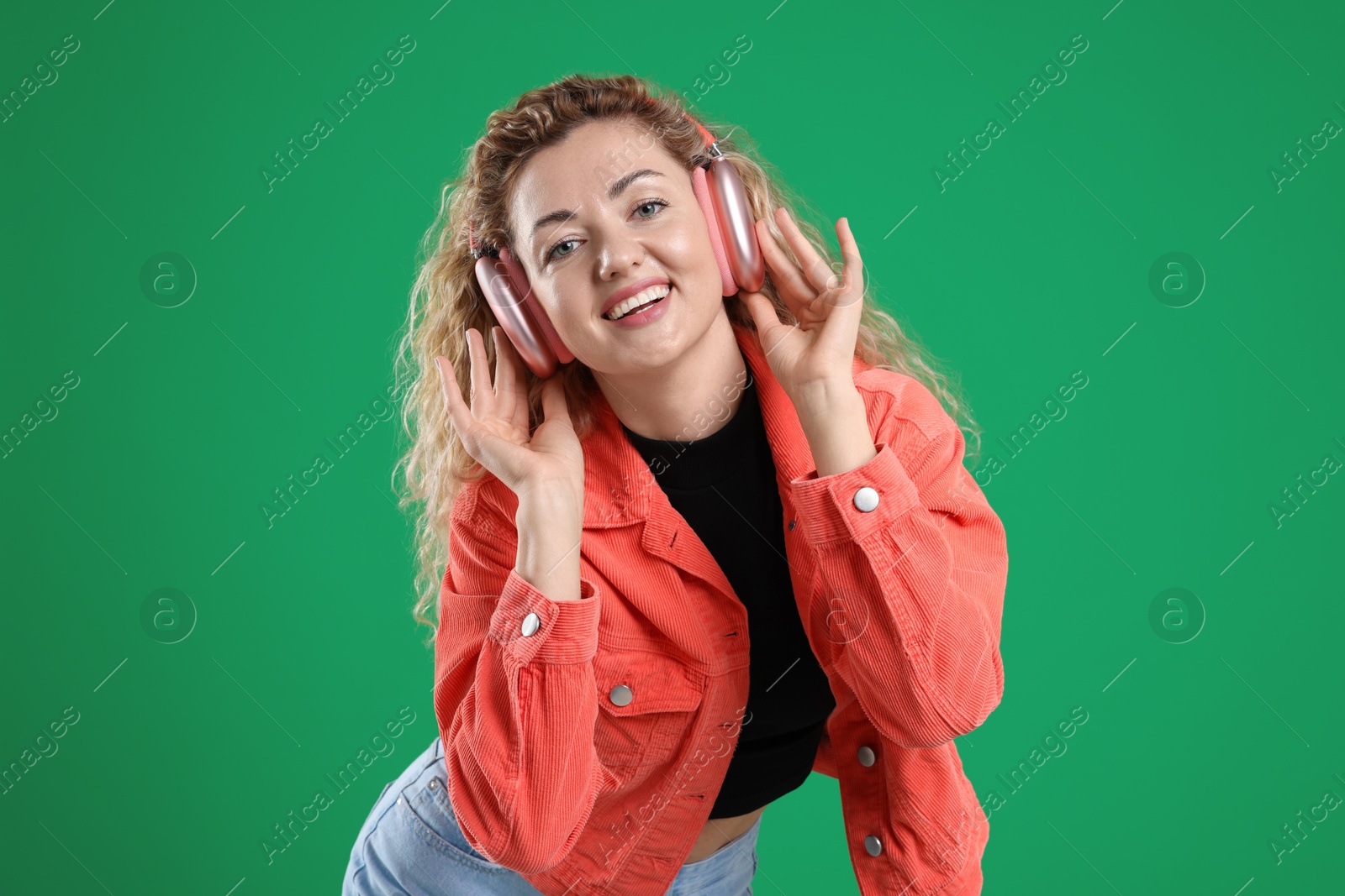 Happy woman listening to music in headphones and dancing on green background Photo of Happy woman listening to music in headphones and dancing on green background