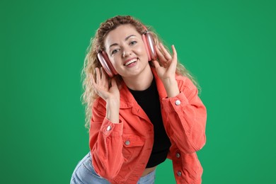 Photo of Happy woman listening to music in headphones and dancing on green background
