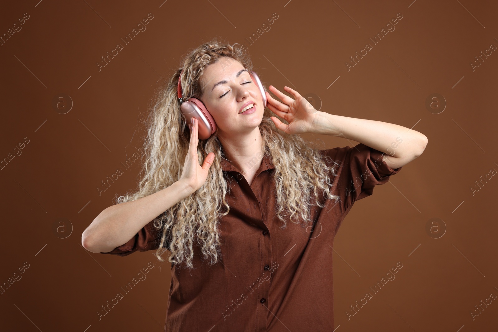 Happy woman listening to music in headphones and dancing on brown background Photo of Happy woman listening to music in headphones and dancing on brown background