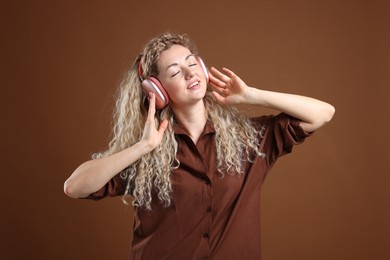 Photo of Happy woman listening to music in headphones and dancing on brown background