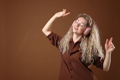 Photo of Happy woman listening to music in headphones and dancing on brown background. Space for text