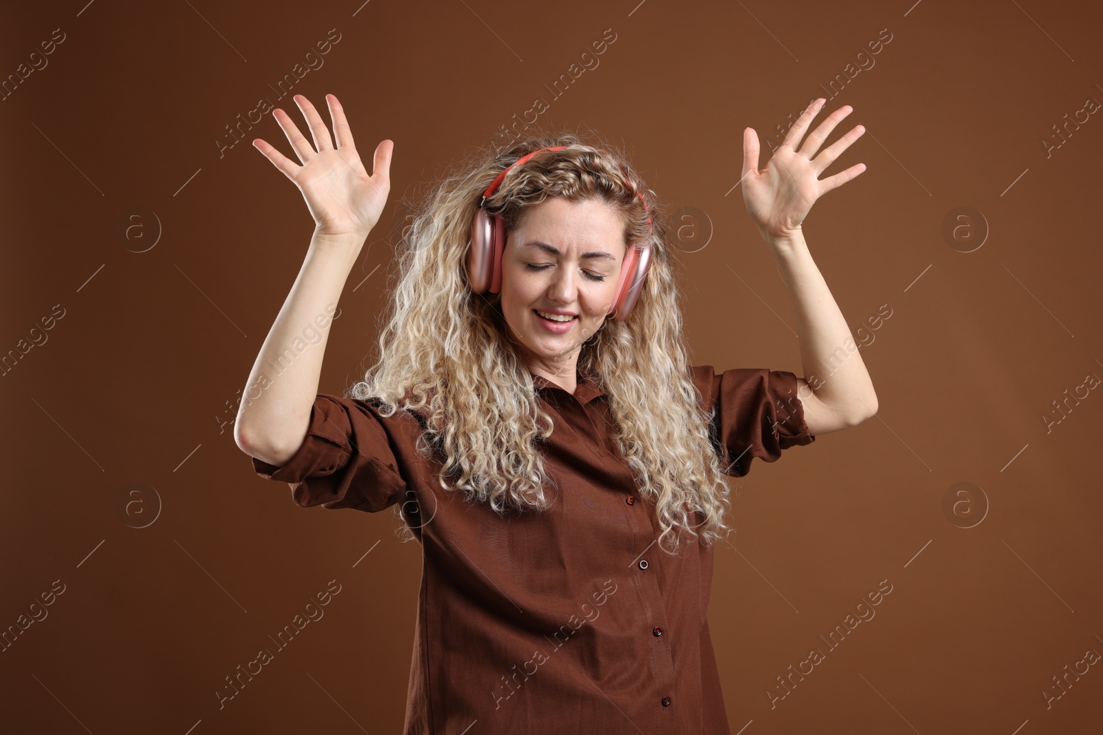 Happy woman listening to music in headphones and dancing on brown background Photo of Happy woman listening to music in headphones and dancing on brown background