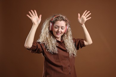 Photo of Happy woman listening to music in headphones and dancing on brown background