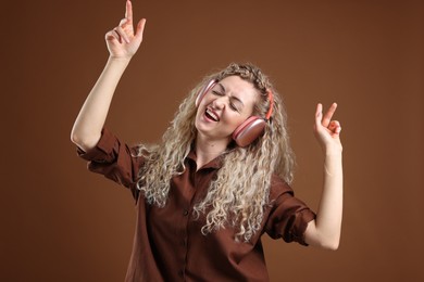 Photo of Happy woman listening to music in headphones and dancing on brown background