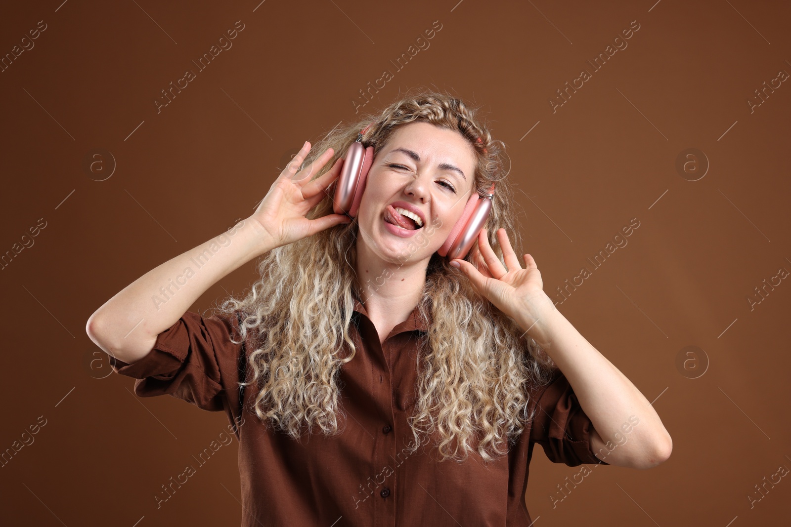 Happy woman listening to music in headphones and dancing on brown background Photo of Happy woman listening to music in headphones and dancing on brown background