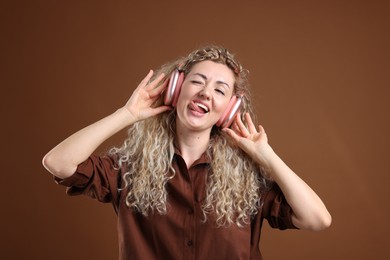Photo of Happy woman listening to music in headphones and dancing on brown background