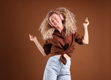 Photo of Happy woman listening to music in headphones and dancing on brown background