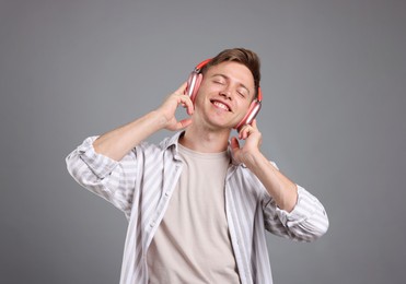 Photo of Happy man listening to music in headphones and dancing on grey background
