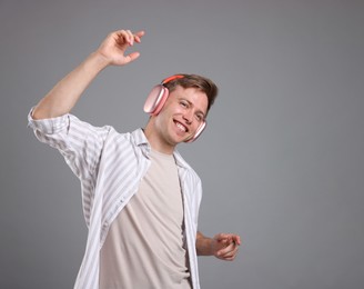 Photo of Happy man listening to music in headphones and dancing on grey background