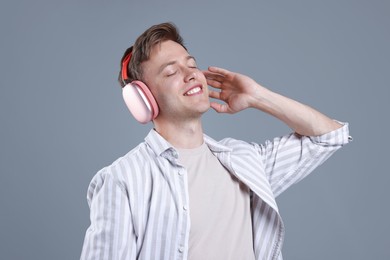 Photo of Happy man listening to music in headphones and dancing on grey background