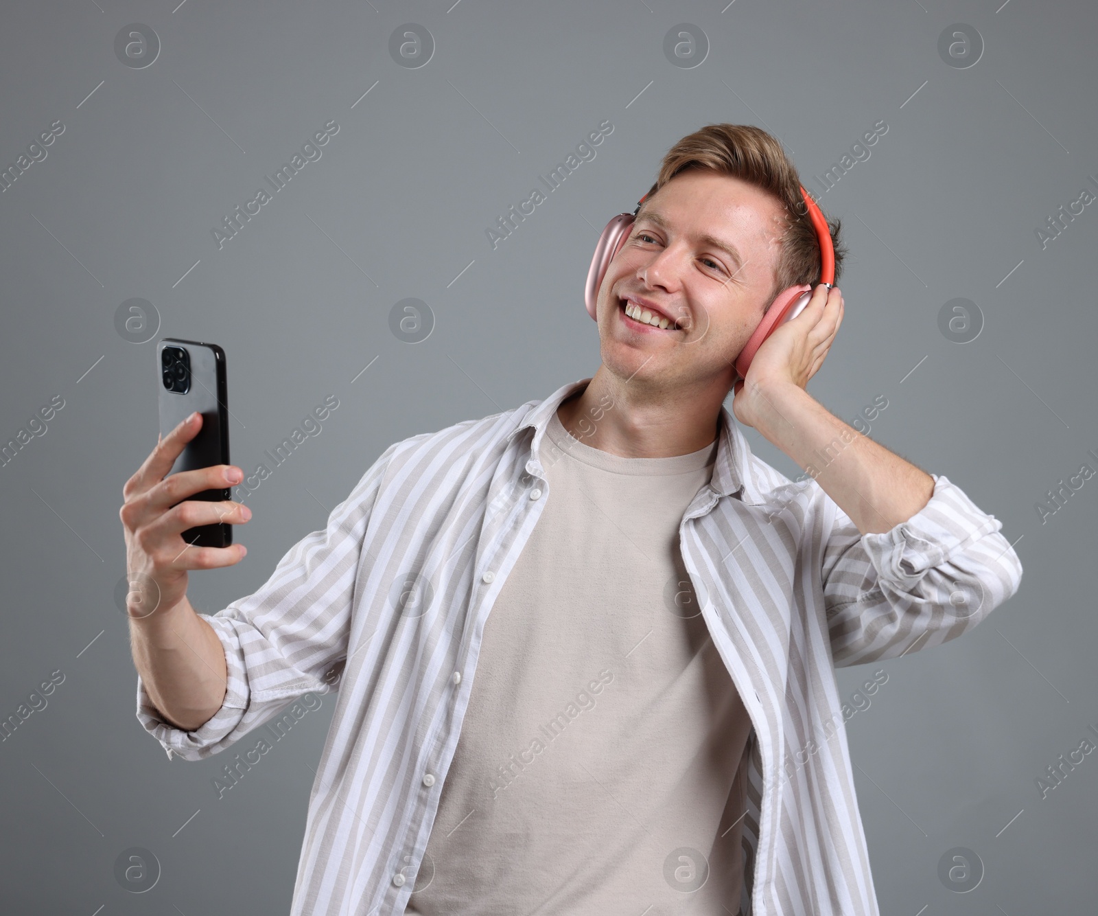 Happy man with smartphone listening to music in headphones on grey background Photo of Happy man with smartphone listening to music in headphones on grey background